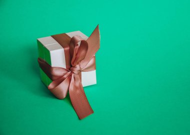 Yeşil arka planda pembe kurdeleli beyaz hediye kutusu. Mesaj için yer. Satışlar, doğum günü, Noel zamanı.