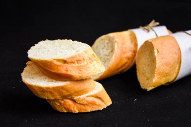 Dilimlenmiş Fransız ekmeği ve koyu arkaplanda kırıntılar.