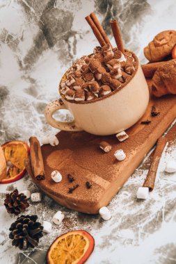 Bir fincan yeni yıl lezzetli sıcak çikolata ve üzerine kakao tozu, koni ve kruvasan serpiştirilmiş kakao gri bir masada tarçın, seçici bir odak noktası.