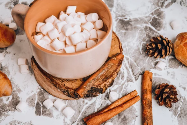 Una taza de Navidad Año Nuevo delicioso chocolate caliente y cacao con malvaviscos salpicados con cacao en polvo, conos y croissants, canela en una mesa gris, enfoque selectivo — Foto de Stock
