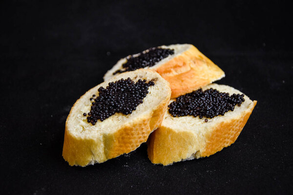 three tasty sandwiches with black caviar on the dark background