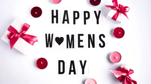 Happy womens day text on white table background, with gift boxes and candles — Stock Photo, Image