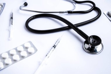 Beyaz zemin üzerinde şırınga ve ilaç bulunan tıbbi steteskop