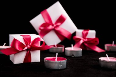 Pembe kurdeleli hediyeler ve siyah arkaplanda mumlar.