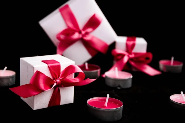 Regalos con cinta rosa y velas sobre fondo negro — Foto de Stock