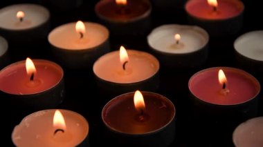 Close-up of burning tealight candle grouped together on black background. Romantic atmosphere