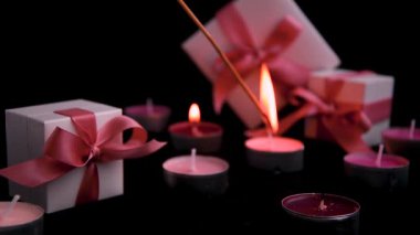 Romantic background: close-up burning tea light candle with present boxes