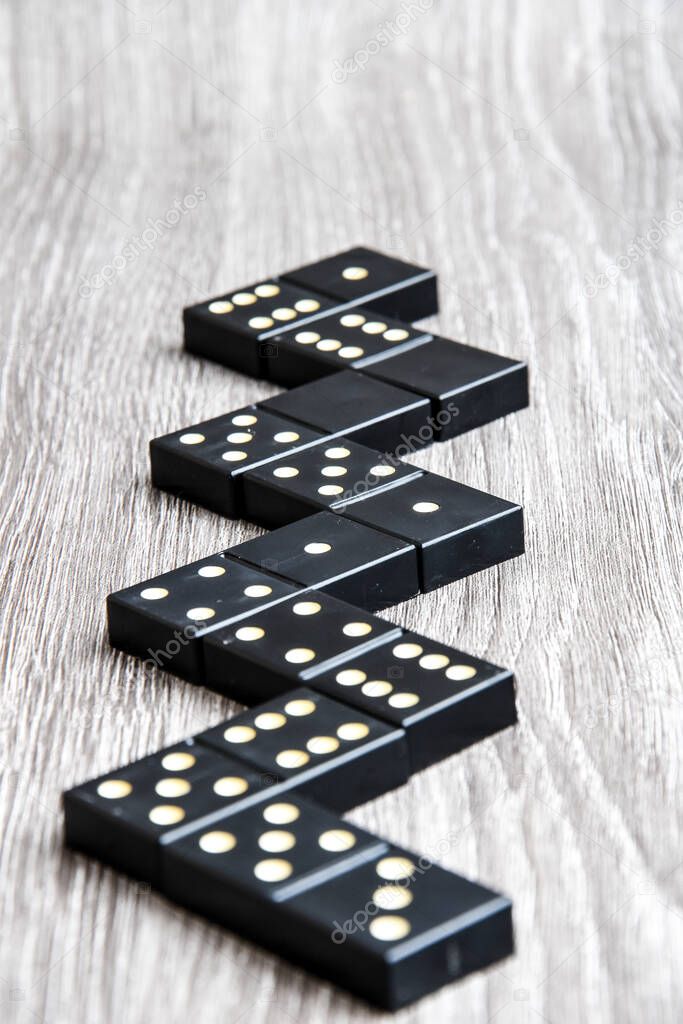black Domino dice on a light wooden table, the process of playing dominoes, selective focus, close up, table game