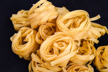 Pasta all 'uovo, Tagliatelle Pasta, siyah zemin üzerinde yuvarlak makarnalar, siyah karatahtanın üzerinde çiğ italyan makarnası fettucine.