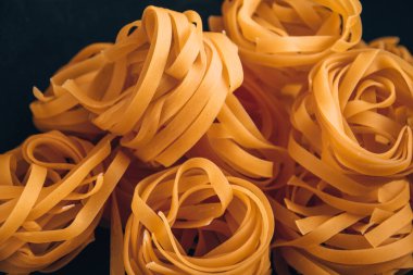 Pasta all 'uovo, Tagliatelle Pasta, siyah zemin üzerinde yuvarlak makarnalar, siyah karatahtanın üzerinde çiğ italyan makarnası fettucine.
