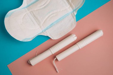 Mavi ve pembe arka planda hijyenik tamponlar ve ped. Fotokopi alanı, regl pedi ve kadın hijyen koruması için tampon. Kritik günler. Mavi arka planda tıbbi gebelik, günlük, adet gören kadın.