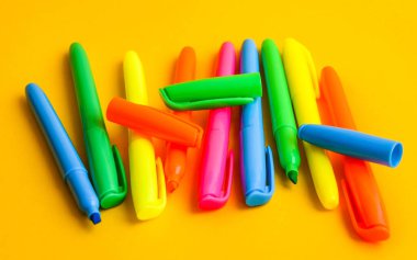 Fotokopi alanı olan sarı arka planda keçeli kalemler, kapakların yanında yeni açılmış renkli keçeli kalemler. Ofis malzemeleri konsepti