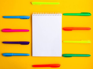 Metin için boş alanı olan not defteri, sarı arkaplanda renkli keçeli kalemler, kopyalama alanı, ofis kaynakları