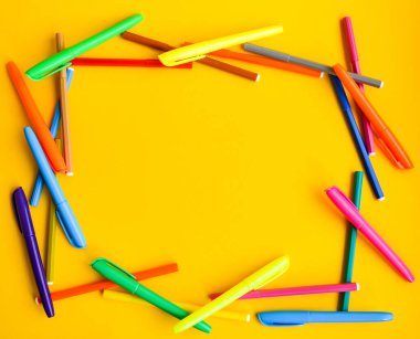 Fotokopi alanı olan sarı arka planda keçeli kalemler, kapakların yanında yeni açılmış renkli keçeli kalemler. Ofis malzemeleri konsepti