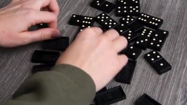 Playing dominoes on a wooden table. Womans hand with domino. Leisure games concept. Selective focus.