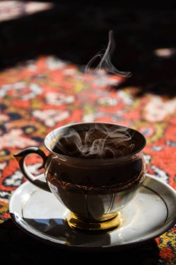 Türkçe halıda klasik porselen çay saati, porselen fincanda siyah çay güneş ışığında çay tabağı, Asya çay seremonisi, sıcak buhar.