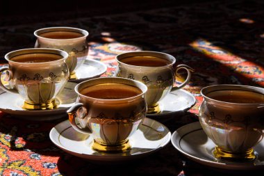 Eski sovyet porselen fincanları, Türk halısı üzerinde çay tabakları, geleneksel çay seremonisi, gölgeli güneş ışığı.