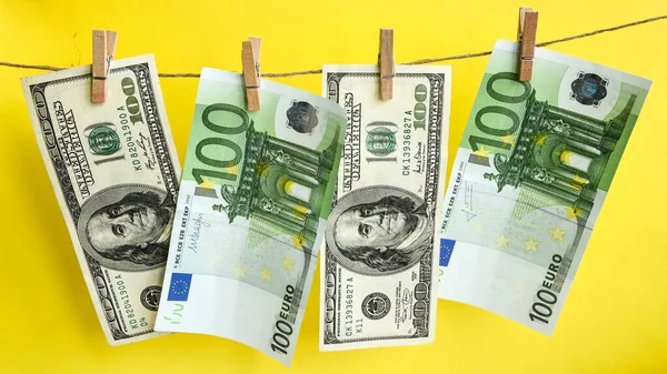 Bir ipe 100 dolar ve euro, sarı arka planda izole edilmiş bir ipe takılmış dolar para aklama konsepti. İpler Euro dolarlarını kuruttu. Yıkandıktan sonra dolar. Dürüstçe kazanılan para. Paranın yasallaştırılması. Hayır demetleri