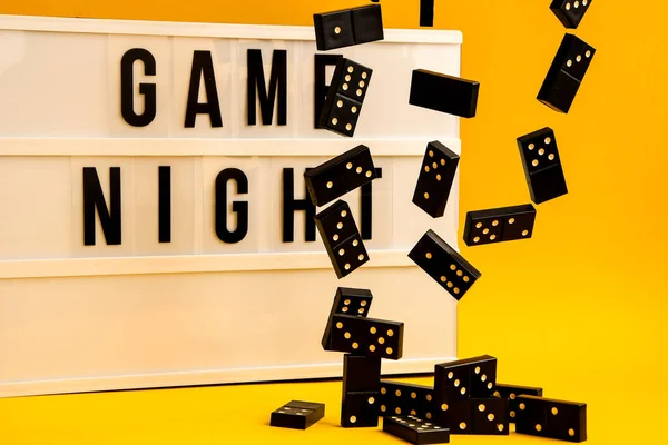 Game night text on lightbox with black dominoes on yellow background, table game, dominoes flying