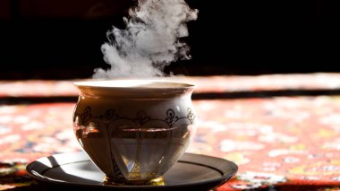 Türkçe halıda klasik porselen çay saati, porselen fincanda siyah çay güneş ışığında çay tabağı, Asya çay seremonisi, sıcak buhar.