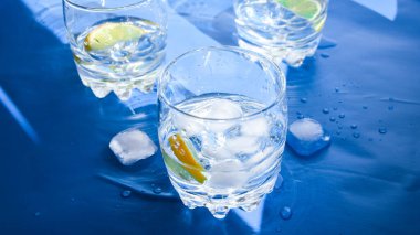 Mavi arka planda buzlu ve limonlu ferahlatıcı su bardakları. Sıcaklık konsepti, taze. Doğal ışık, fotokopi alanı, yaz sıcağı