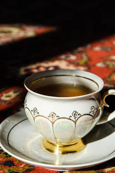 老式瓷茶时间在土耳其地毯上，红茶在瓷杯中烟熏，茶碟在阳光下，热蒸汽 — 图库照片