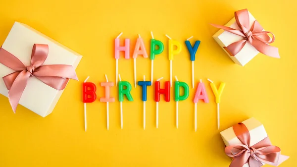 Velas de aniversário feliz no fundo amarelo. Velas de papel de parede de cor brilhante com texto feliz aniversário presentes caixas — Fotografia de Stock