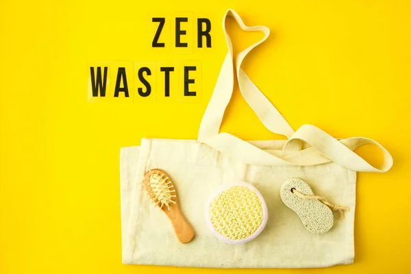 Zero waste concept. Textile eco bags, glass jars, wooden hair brush and washcloth on yellow background with Zero Waste black text in center. Eco friendly and reuse concept. Top view or flat lay