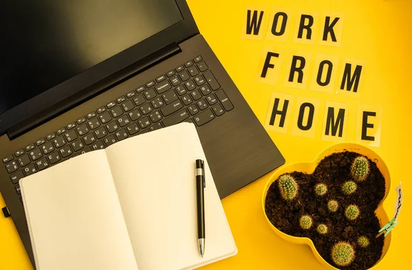 Text WORK FROM HOME with notebook, laptop and pen, cactus, work from home place, freelance environment on yellow background copy space, planning day, to do list