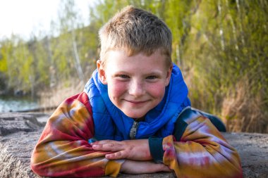 Küçük çocuk ormanın yanında oynadıktan sonra taşın üzerinde dinleniyor.