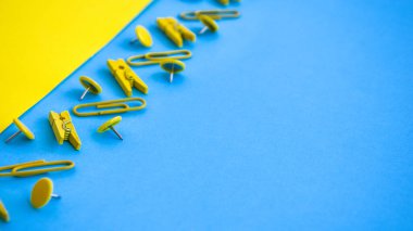 Ofis malzemeleri renkli düğmeler ve ataçlar şeklinde, sarı ve mavi arkaplanda mandallar, kopya alanı, sınır ve çerçeve, okul konseptine geri dönüş