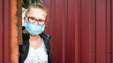 Tıp maskeli okul çağındaki çocuklar. Liseli kız portresi çitin arkasından izliyor ve bakıyor, 2020 numaralı karantina, Coronavirus covid 19