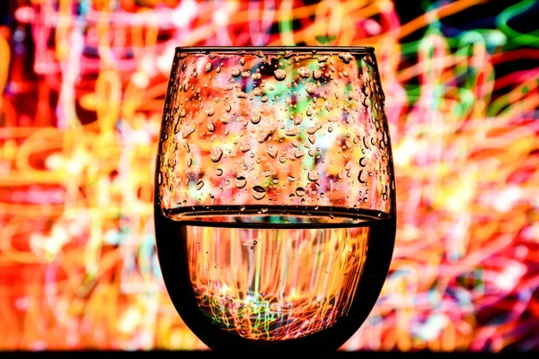 wine glass with colorful light painting behind, luxury splash drink in a glass on a high leg on a colored background, alcoholic drink bar concept