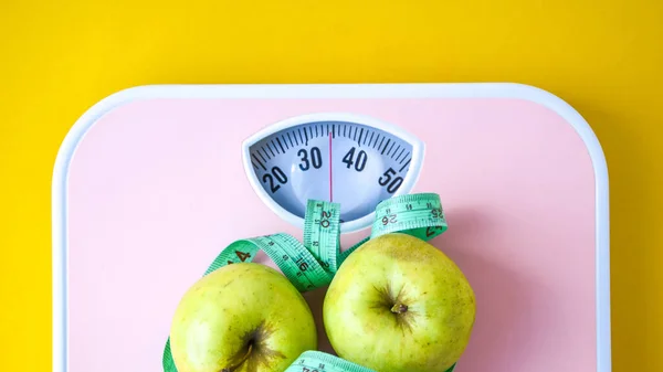 Green Apple with measuring tape and pink Weight scales. Concept of health care, fitness at home, diet