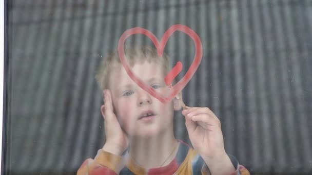 Cuarentena. El niño dibuja el corazón rojo en la ventana con pintura. Esperando el arco iris, Quédense en casa — Vídeos de Stock