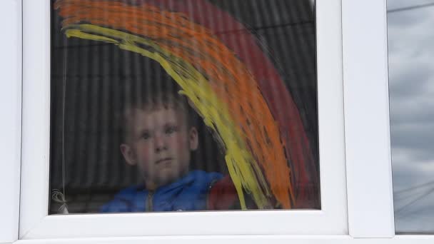 Мальчик рисует радугу на окне во время карантина Ковид-19 дома. Кампания в социальных сетях Stay at home по профилактике коронавируса, позволит всем быть здоровыми — стоковое видео