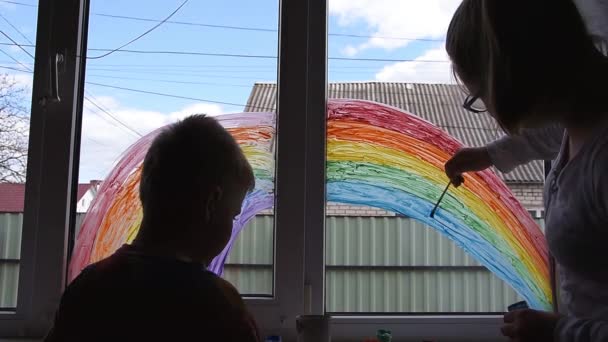 Chica y niño pintando arco iris en la ventana durante la cuarentena de Covid-19 en casa. Permanecer en casa campaña de medios sociales para la prevención del coronavirus — Vídeo de stock