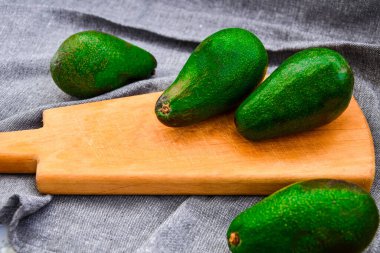 Ahşap tepside yeşil avokado, gri mutfak havlusu, vejetaryen vejetaryen yemeği, sağlıklı beslenme, diyet konsepti.