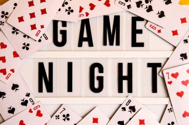 Sarı arkaplanda oyun kartları, masa oyunları, masa oyunları ve sarı arkaplanda Scrabble harfleri olan ışık kutusundaki oyun gecesi metni Oyun Gecesi