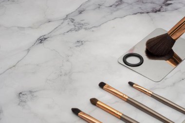 Brocha de maquillaje grande, junto a otras bochas mas pequeas, con una espatula sobre una base de mrmol