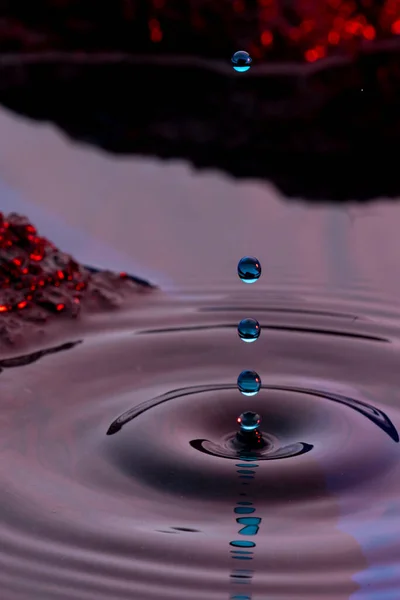 Drops of water captured on the shore of a lake at sunset forming ripples in the lake and with the rocks in the background receiving sunlight