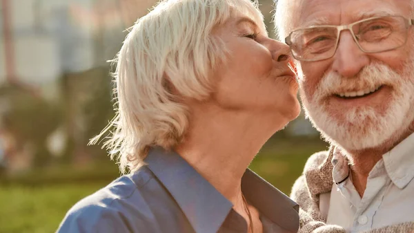 Schöne Seniorin küsst ihren Mann auf die Wange, während sie gemeinsam im Park steht — Stockfoto