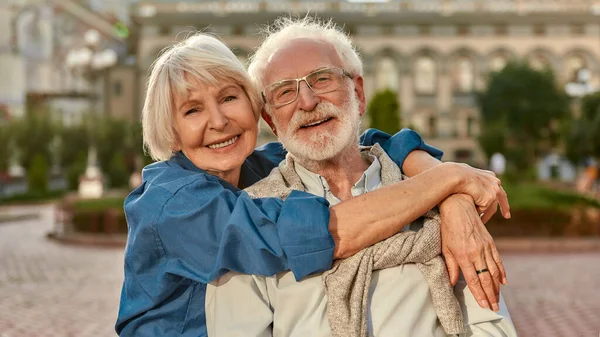 Ich liebe meinen Mann. Porträt eines fröhlichen Seniorenpaares in lässiger Kleidung, das sich umarmt und lächelnd in die Kamera schaut, während es draußen zusammen steht — Stockfoto