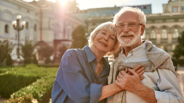 Porträt eines schönen, glücklichen Seniorehepaares, das sich aneinander klammert und Händchen hält, während es gemeinsam im Park steht — Stockfoto