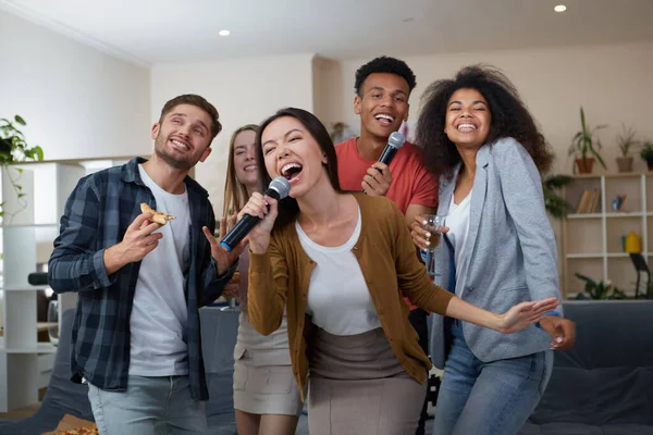 Gadis asia muda memegang mikrofon dan bernyanyi sambil bermain karaoke dengan teman-teman terbaik di rumah. Sekelompok orang bersenang-senang bersama, minum dan makan pizza. Pesta karaoke — Stok Foto