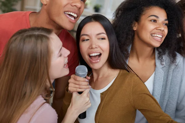 Pesta karaoke. Kelompok muda dan bahagia multikultural teman-teman dalam pakaian kasual bernyanyi dengan mikrofon bersama-sama saat bermain karaoke di rumah. Persahabatan. Hiburan rumah — Stok Foto