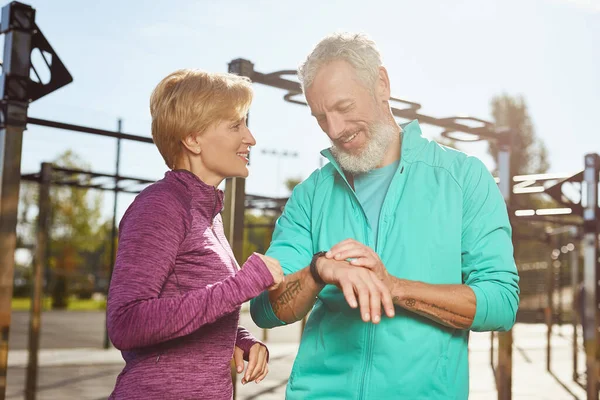 Fitness-App. Glückliches reifes Familienpaar in Sportkleidung überprüft Trainingsergebnisse beim gemeinsamen Training im Freien, schaut auf die Smartwatch und lächelt — Stockfoto