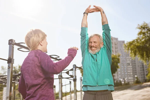 Gesunder Lebensstil. Schönes älteres oder reiferes Familienpaar in Sportbekleidung, das frühmorgens im Outdoor-Fitnessstudio gemeinsam Dehnübungen macht — Stockfoto