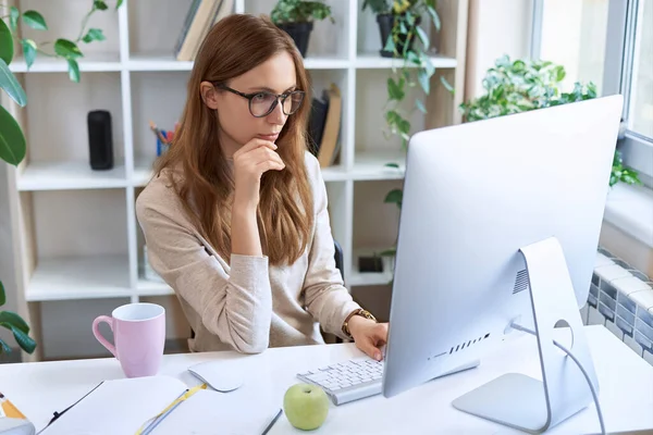 Online arbeiten. Junge, konzentrierte Geschäftsfrau, attraktive Angestellte mit Brille, die am Schreibtisch sitzt und zu Hause am Computer arbeitet — Stockfoto