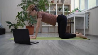Spor ve kendini izole etme. Güzel genç bir kadın yoga yapıyor ya da evde yerde geriniyor. Dizüstü bilgisayarında video dersi izliyor.